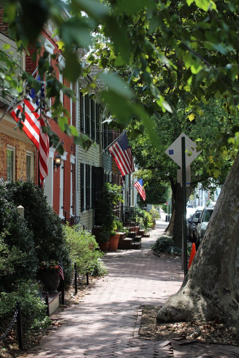 Brick sidewalk under shade trees past historic row houses with American flags in Annapolis, Maryland